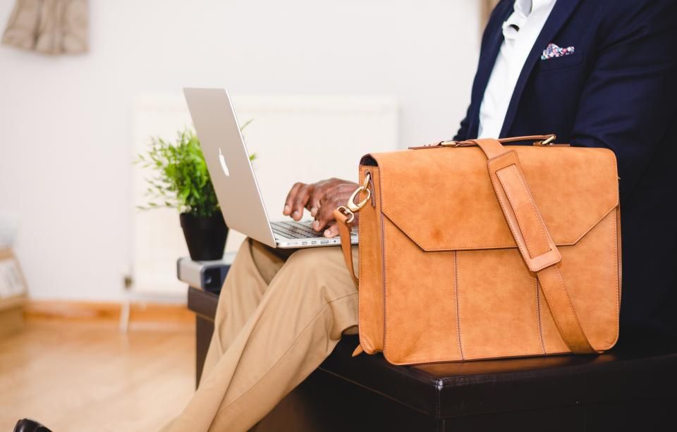 Person in a navy suit working on a laptop beside a leather briefcase